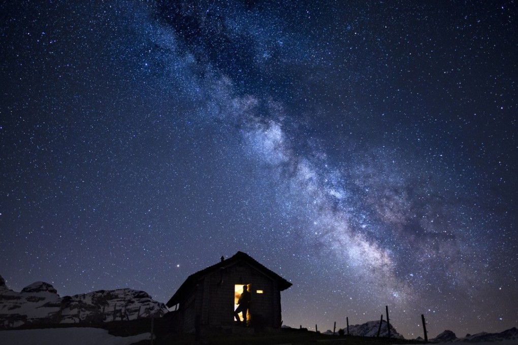 A man is silhouetted against the illuminated inside of a small cabin with a view of the Milky Way dominating the sky over the Ormont Valley, Switzerland. Photo: EPA