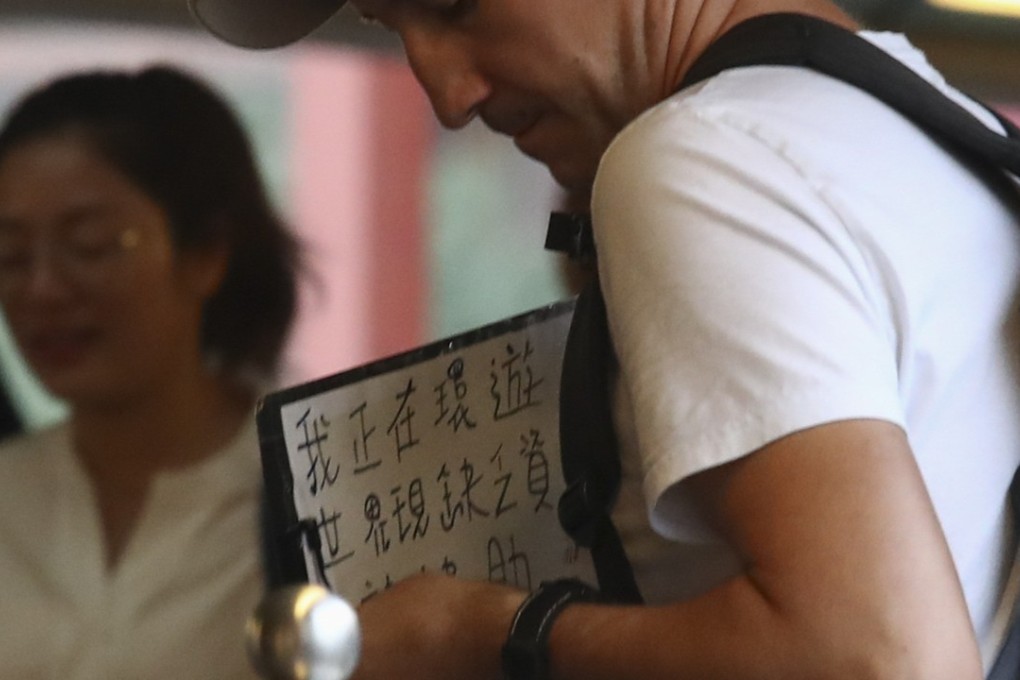 A man holds a sign in Chinese asking for money to support his travels. Photo: Nora Tam
