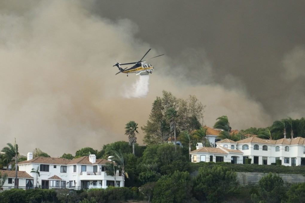 A helicopter drops water on a brush fire behind homes during the Woolsey Fire in Malibu. Photo: AP