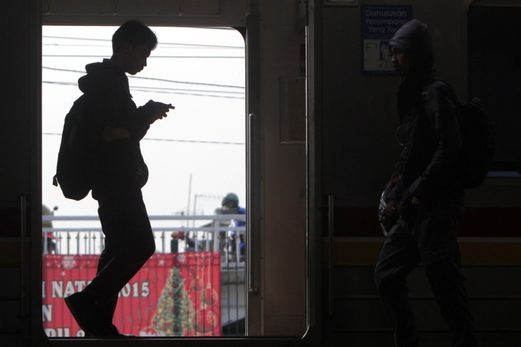 An Indonesian worker holds a mobile phone inside a train in Jakarta, Indonesia in 2016. The prevalence of mobile technology in Southeast Asia has raised concerns about affordability of high-speed internet. Photo: EPA