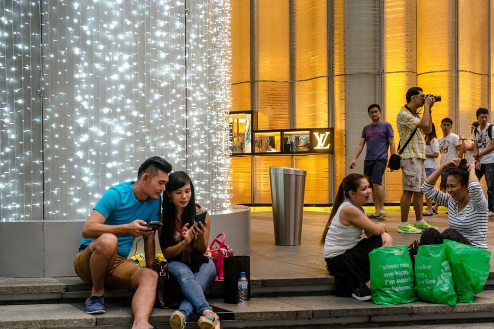 Shoppers sit on a set of steps outside a LVMH Moet Hennessy Louis Vuitton SA store on Orchard Road in Singapore, on Sunday, Dec. 16, 2016. Shopping has overtaken gambling as the biggest earner in Singapore's tourism industry for the first time since 2012, surging 44 percent in the six months through June from a year ago, official data show. Photographer: Sanjit Das/Bloomberg