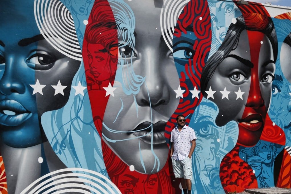 A man poses for a photo in front of a building covered with a mural by US artist Tristan Eaton in the Wynwood district during Art Basel in Miami, Florid. Photo: EPA-EFE