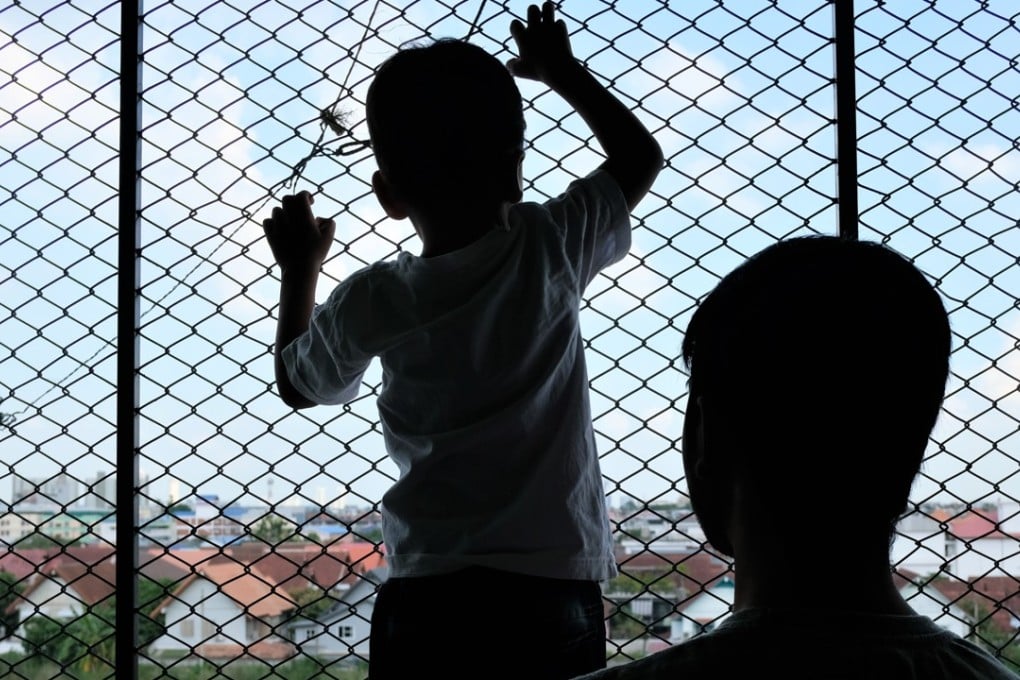 Shazee, a four-year-old stateless boy, gazes through wire-mesh netting in the corridor of a low-rent apartment building in Bangkok, alongside his father, Shan, a Christian asylum seeker from Lahore, Pakistan. Photo: Tibor Krausz