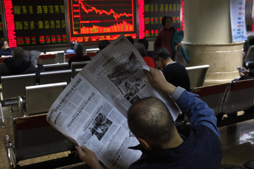 A man reads a newspaper at a brokerage in Beijing on Friday, December 14, 2018. Contrary to global conventions, China’s stock market denotes gains in red, and uses the green colour to illustrate losses. Photo: AP