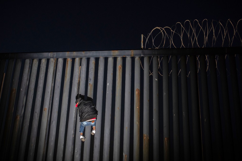 A man climbs up a section of a US-Mexico border wall at night in Tijuana, Mexico, on November 18. Photo: Bloomberg