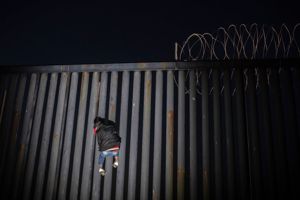 A man climbs up a section of a US-Mexico border wall at night in Tijuana, Mexico, on November 18. Photo: Bloomberg