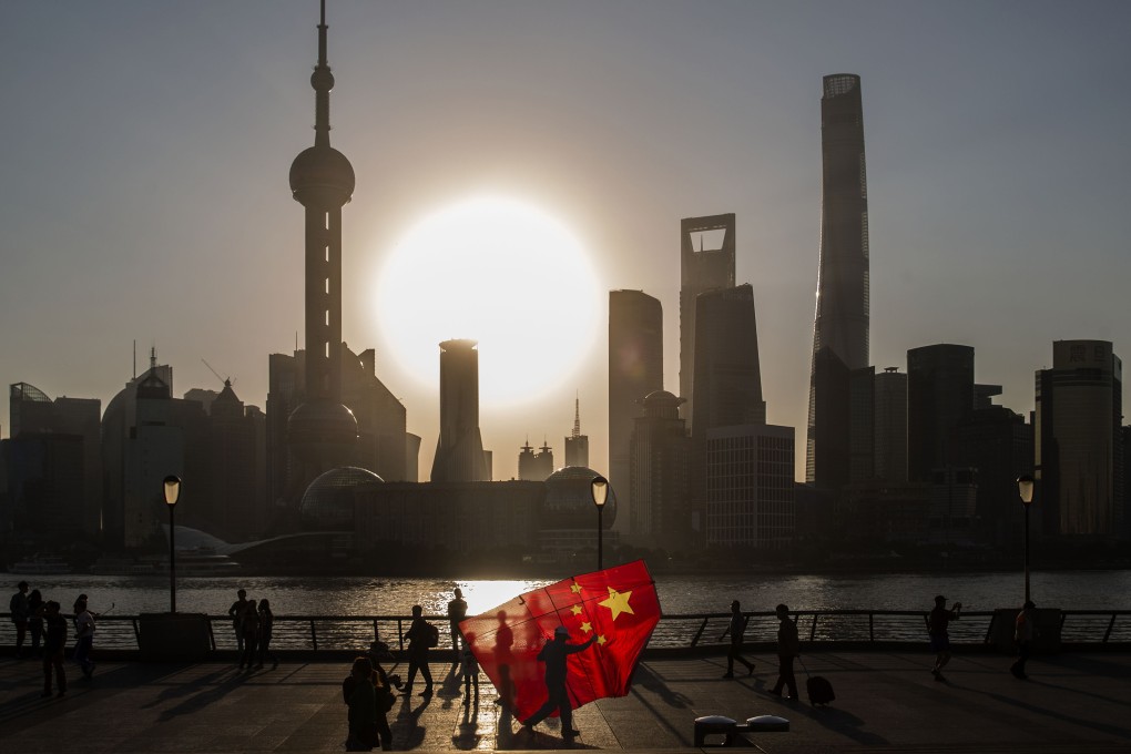A man carrying a kite in the form of the Chinese national flag walks along the Bund, as the sun rises over the buildings of Pudong's Lujiazui financial district, across the Huangpu River, in Shanghai. Photo: Bloomberg