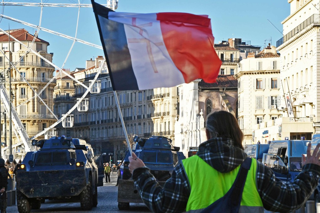 A protestor wearing a "yellow vest" (gilets jaunes) and brandishing a French national flag stands in front of riot police armoured vehicles in Marseille during a protest against rising costs of living on December 8, 2018. Photo: AFP