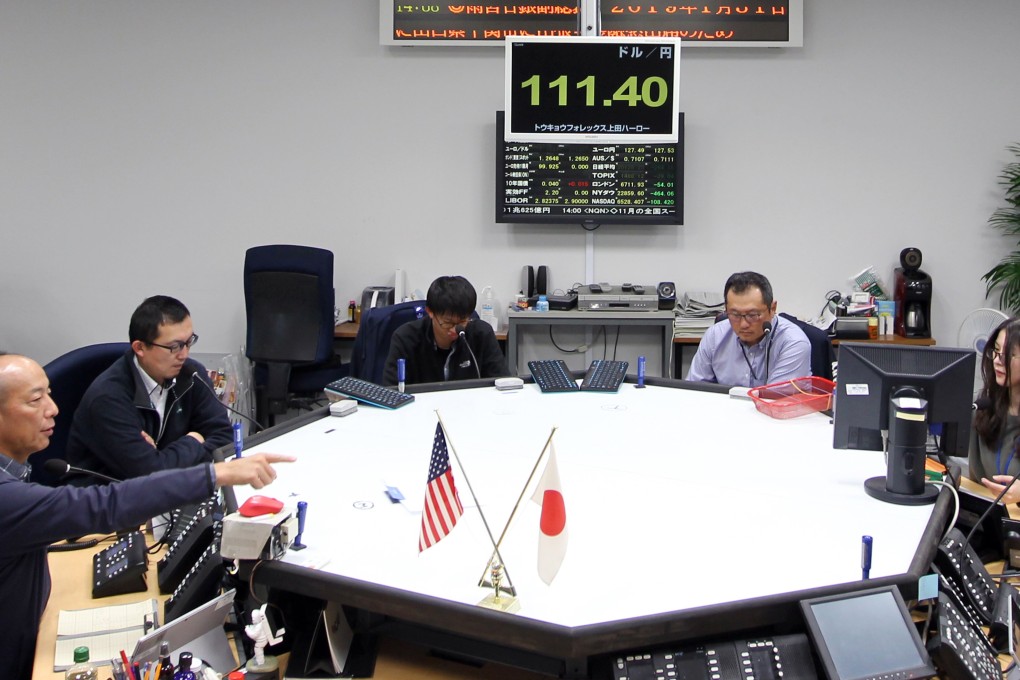 Employees work below a monitor, top, displaying the exchange rate of the yen against the US dollar in the dealing room of the Tokyo Forex & Ueda Harlow foreign exchange brokerage in Tokyo on Friday, December 21, 2018. Photo: Bloomberg