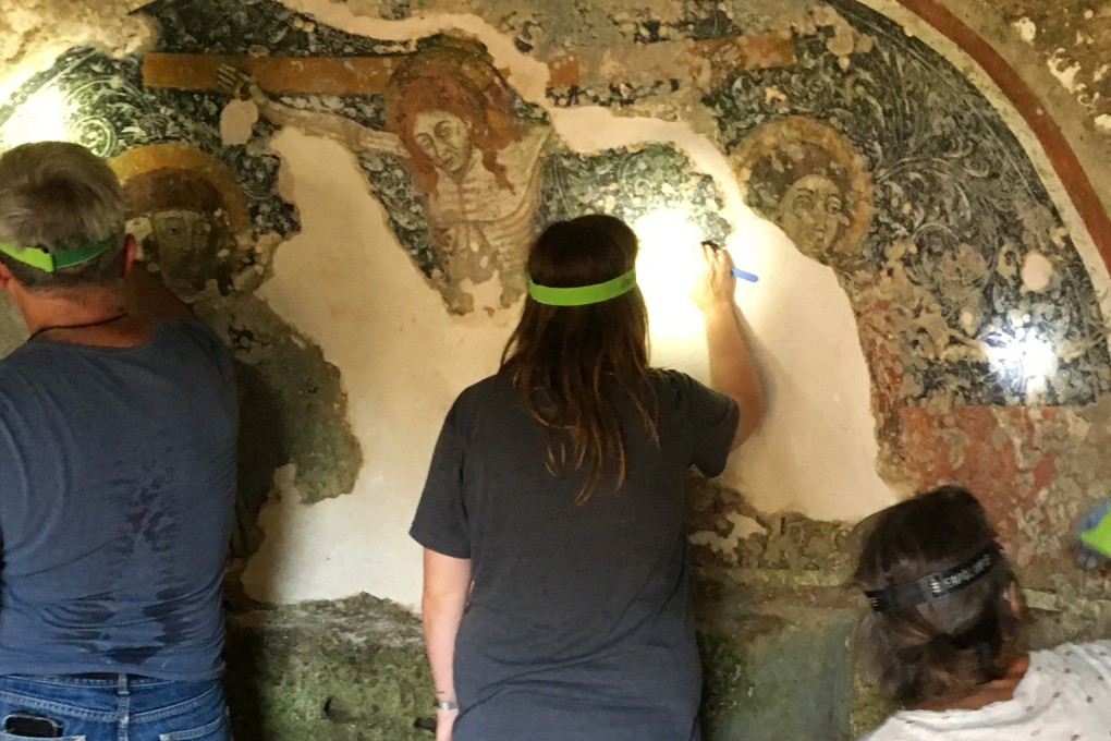 Tonio Creanza (left) and Messors participants remove calcified deposits from a crucifixion fresco in Puglia, Italy. Photo: Ben Yagoda for The Washington Post