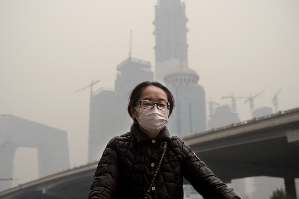 A woman wearing a protective pollution mask cycling in Beijing through thick smog. Photo: AFP