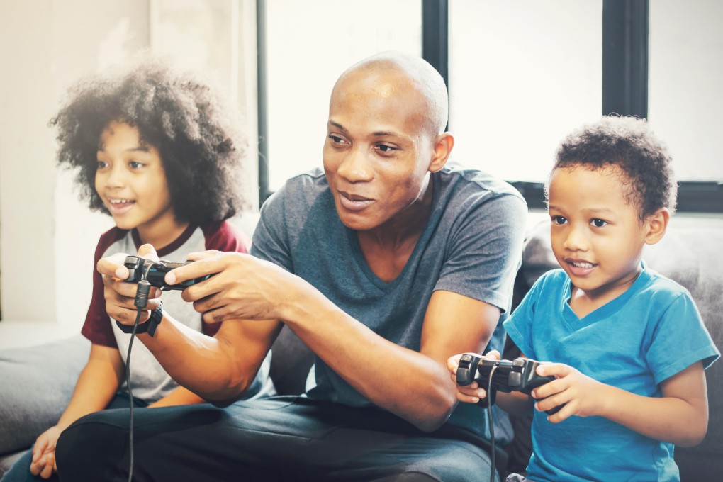 African American family at home sitting in sofa couch and playing console video games together. [20AUGUST 2018 FEATURES] CREDIT: ALAMY