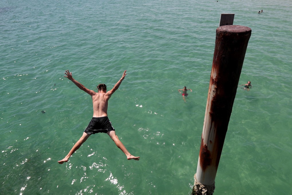 Teens jump of the jetty at Glenelg beach during a hot day in Adelaide, South Australia. Photo: EPA