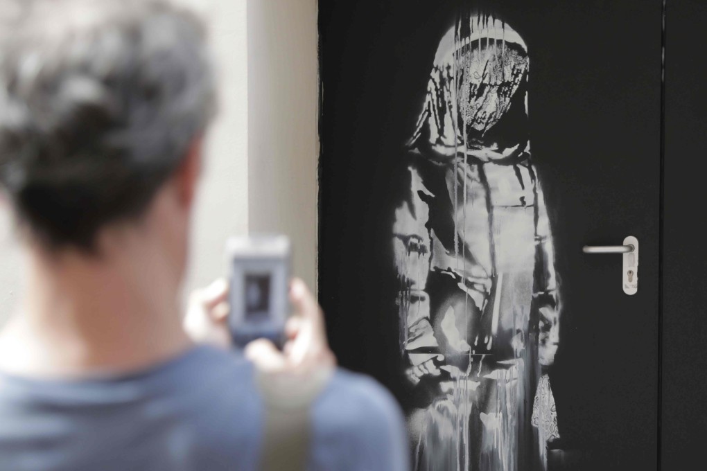 In this file photo taken on June 25, 2018, a man takes a photograph of an artwork by street artist Banksy in Paris on a side street to the Bataclan concert hall where a terrorist attack killed 90 people on November 13, 2015. Photo: AFP