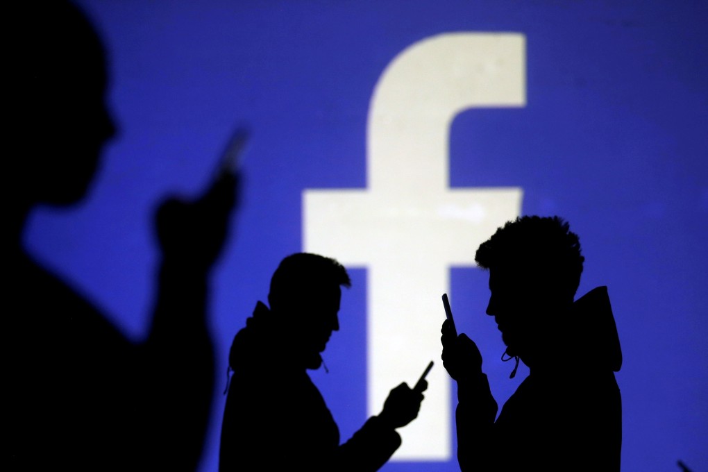Silhouettes of mobile users are seen next to a screen projection of Facebook logo in this picture illustration taken March 28, 2018. Photo: Reuters