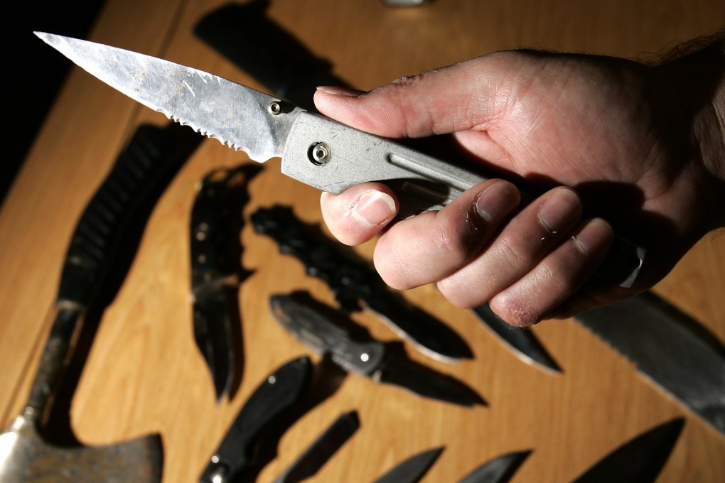 A police officer holds a lock knife over a selection of dangerous weapons seized by authorities. Photo: Reuters