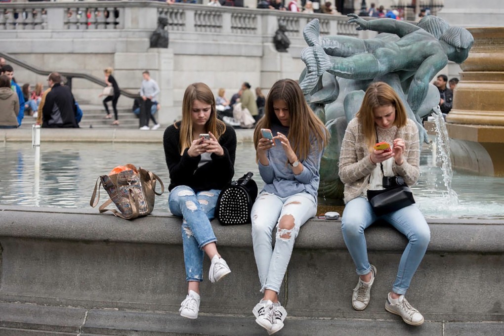 Three teenage girls lost in the world of smartphone apps and messaging in Trafalgar Square, London. Photo: Alamy