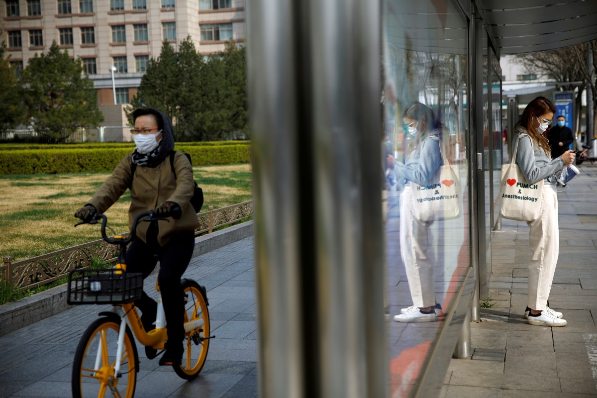 People wear face masks near a bus stop on a street following an outbreak of the coronavirus disease in Beijing on March 30, 2020. Photo: Reuters
