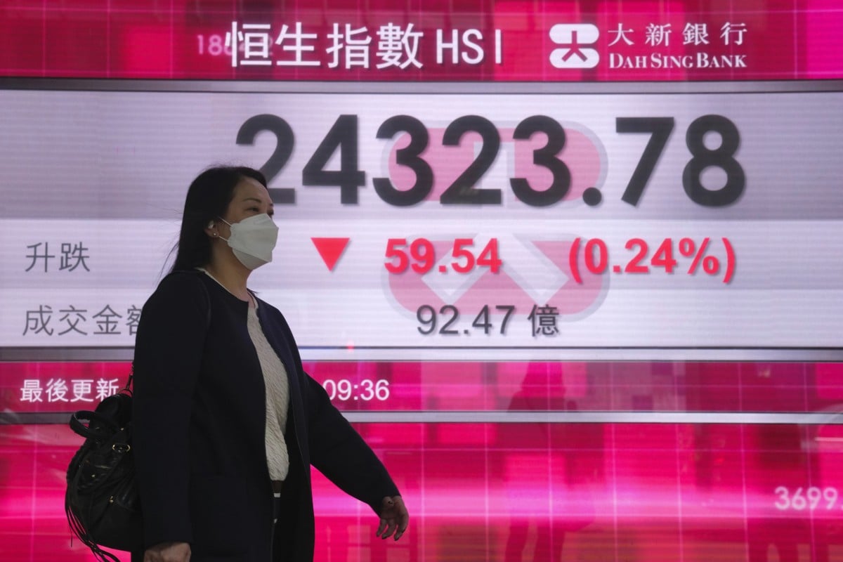 A woman wearing a face mask walks past a bank’s electronic board showing the Hang Seng Index on January 17. Photo: AP