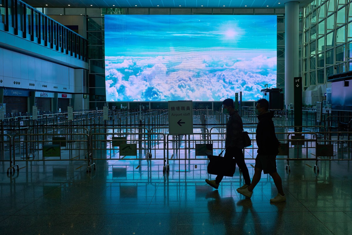 Airport workers walk past a giant screen at an almost deserted Hong Kong International Airport on March 24, 2022. Photo: SOPA Images / LightRocket via Getty Images