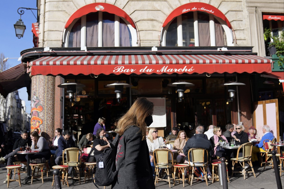 A woman wearing face mask walks in front of an open Parisian cafe in France in March. Photo: AP