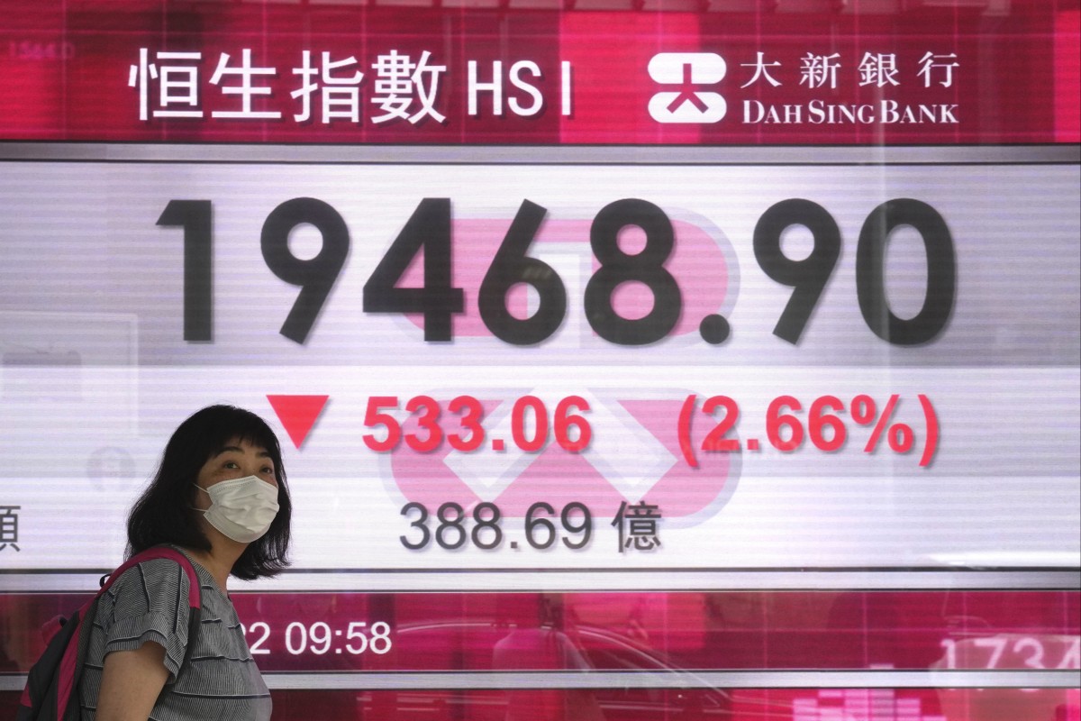 A woman wearing a face mask walks past a bank’s electronic board showing the Hong Kong share index in Hong Kong. Photo: AP Photo