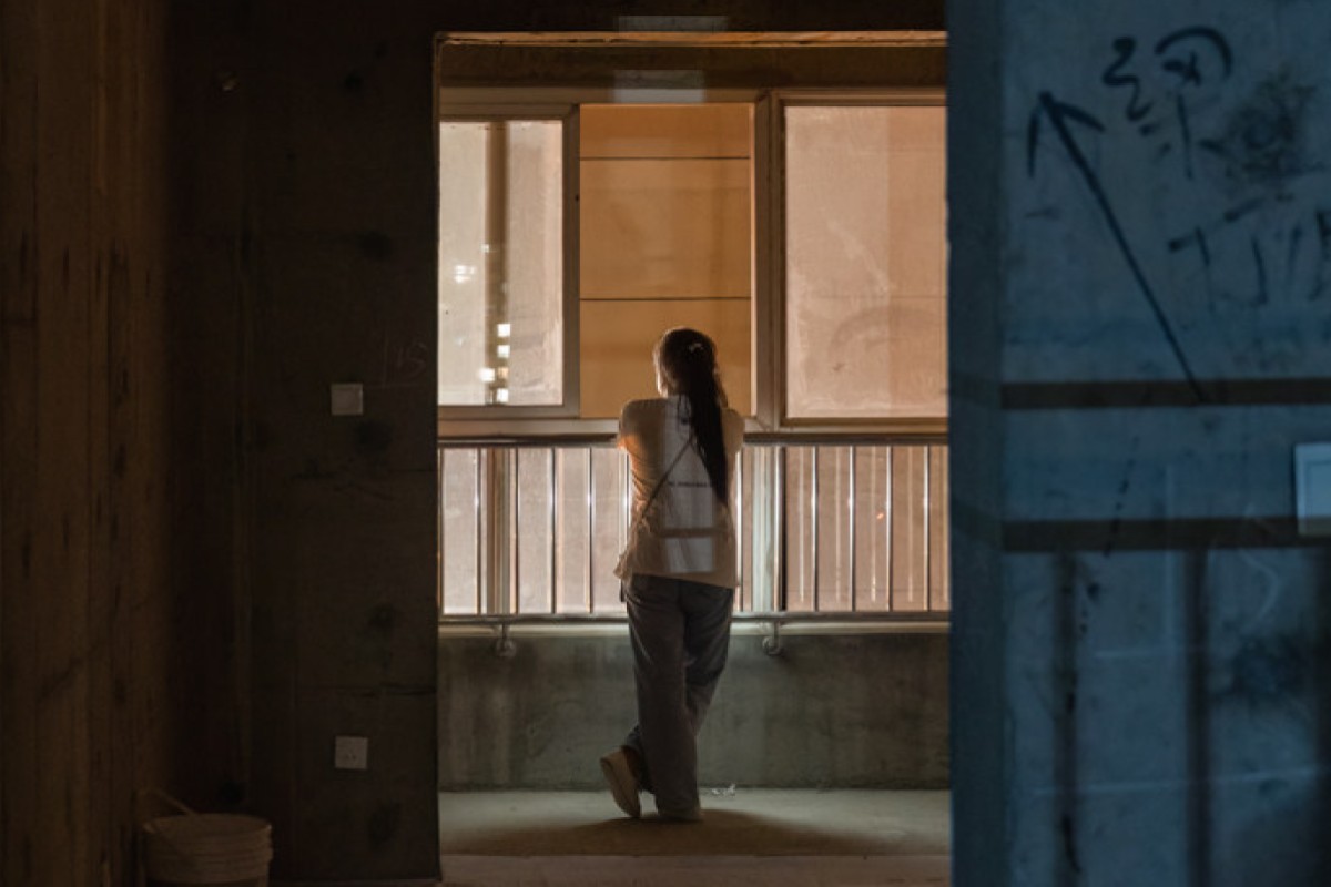 A woman stares out of her unfinished apartment in China in one of the photographs Weimin Chu shot for his series “Faint Light in the Unfinished Building”.   Photo: Weimin Chu