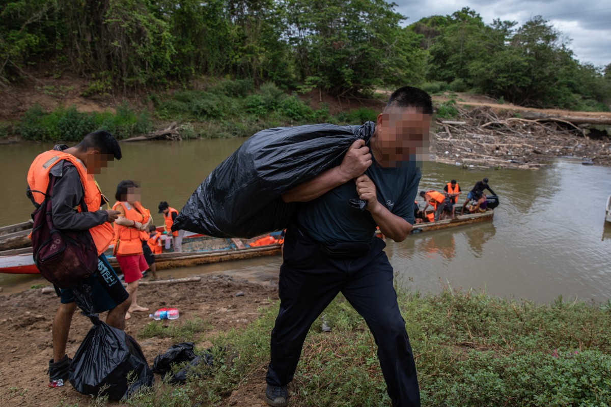 Chinese migrant Cai Fei carries a black plastic bag of his belongings as he steps off the boat and finishes his trek in the Darien Gap, on his journey to the US, in 2023. Photo: Shawn Yuan