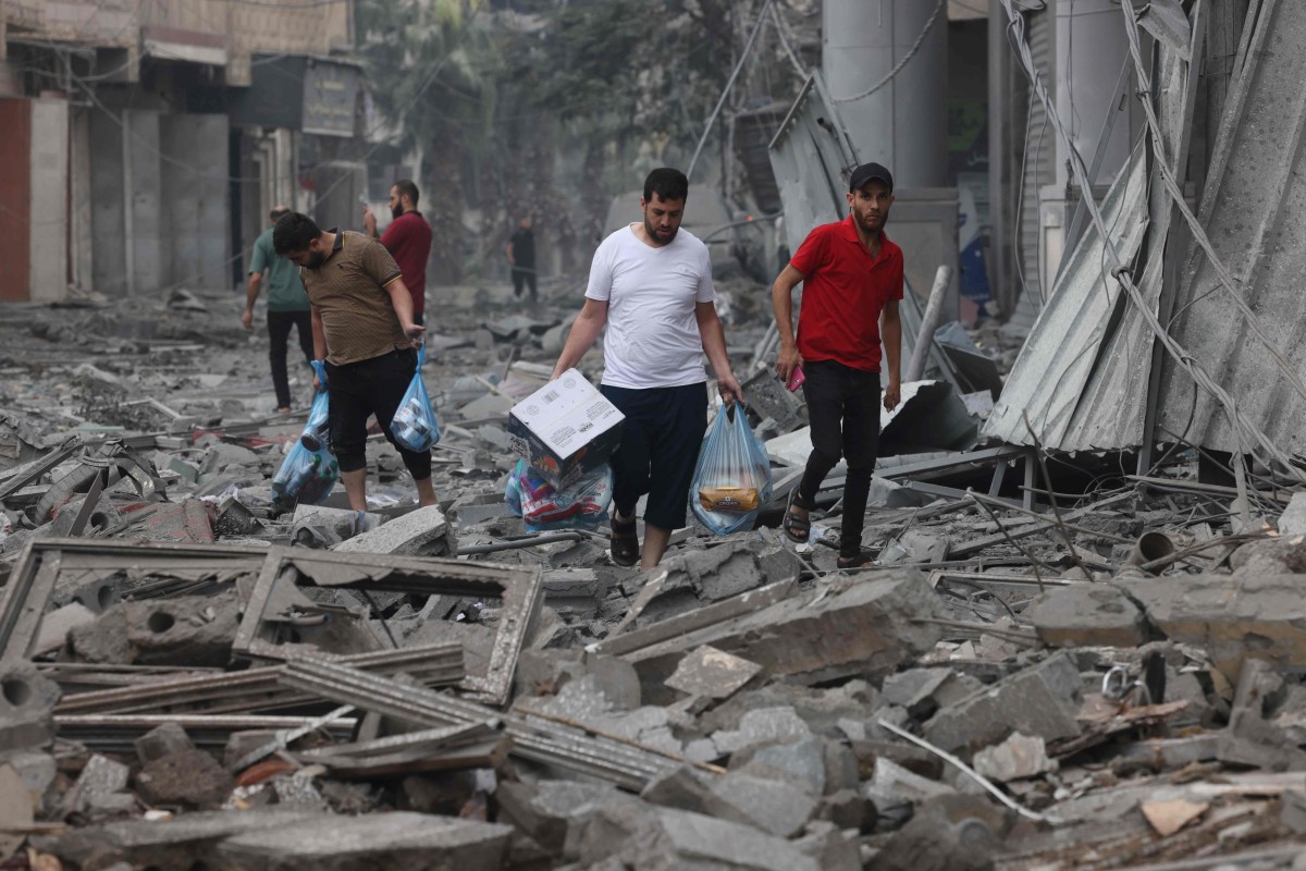 Palestinian men carry food supplies as they walk through debris in Gaza City. Photo: AFP