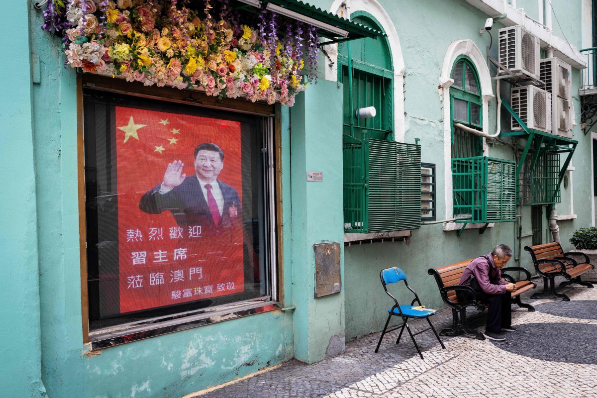 A man sits in an alley next to a screen with the image of China's President Xi Jinping in Macau on December 19, 2019 as the city marks the 20th anniversary of the handover from Portugal to China. Photo: AFP