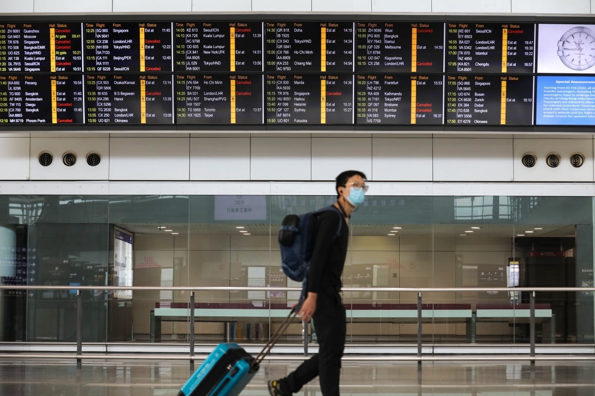 Passengers wearing protective masks walk past an information board at Hong Kong International Airport, on the first day of a travel ban on travellers from South Korea. Photo: Winson Wong