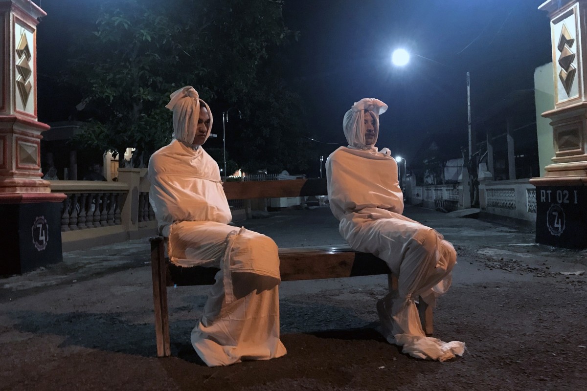 Volunteers play the role of ‘pocong’ to make people stay at home outside the gate of Kepuh village amid the spread of coronavirus in Indonesia. Photo: Reuters