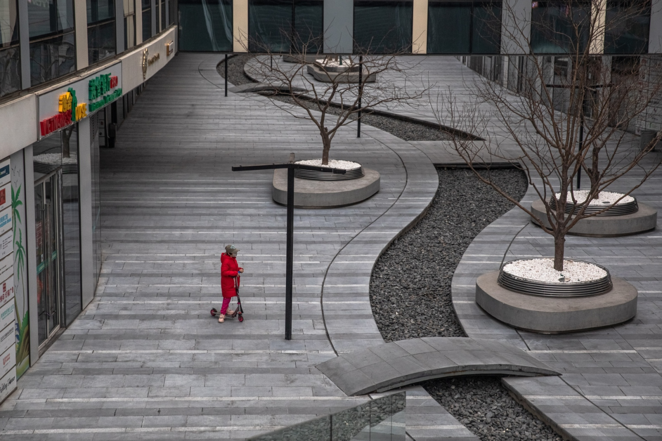 A child wearing a face mask rides on a scooter next to closed shops in an empty shopping and residential area of Sanlitun in Beijing on February 26. (Picture: Roman Pilipey/EPA-EFE)
