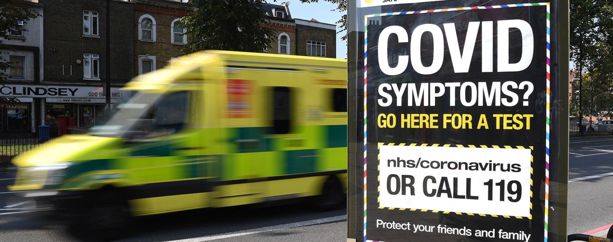 An ambulance drives past a Covid-19 helpline sign in south London. Photo: EPA-EFE