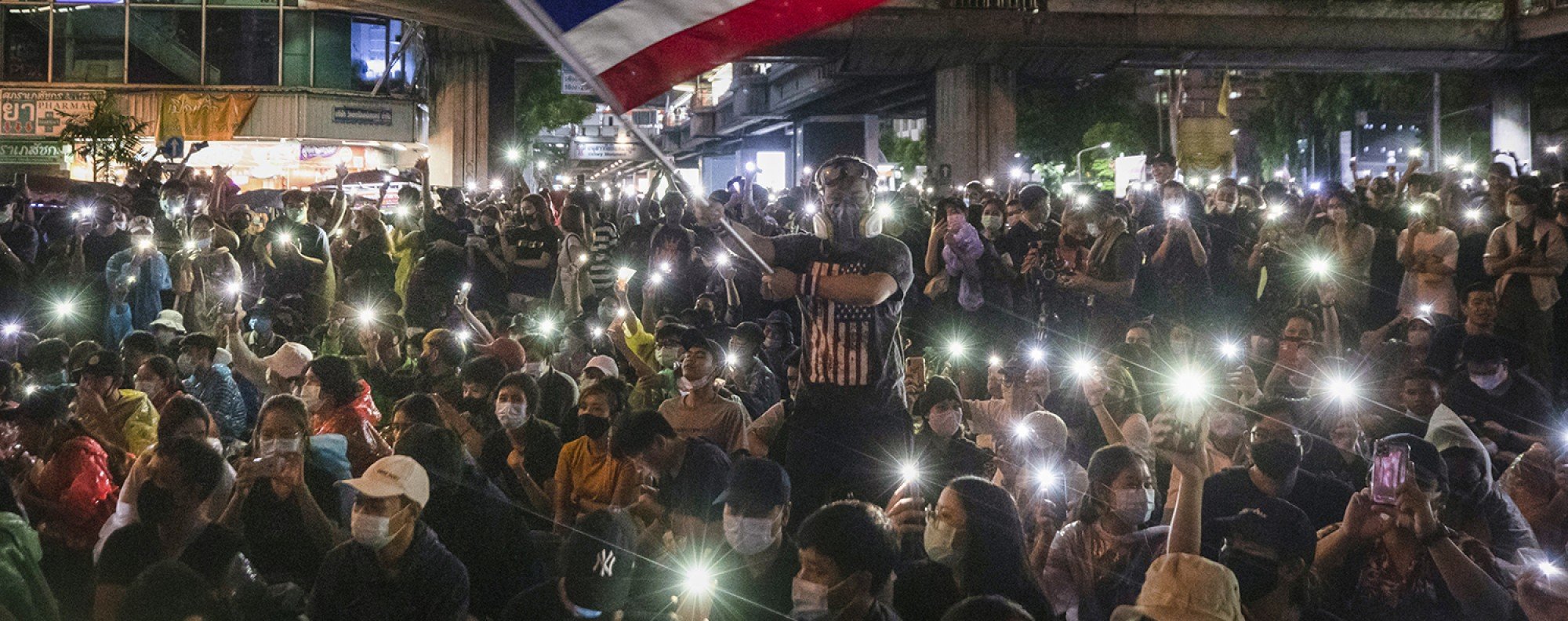 Pro-democracy protesters waves Thailand national flag as others shine their mobile phone lights during an anti-government protest in Bangkok, Thailand. Photo: AP