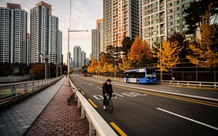 A cyclist rides past residential buildings along a main road as the sun sets in Seoul on November 11. Photo: AFP