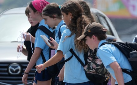 A girl uses her phone as she walks with a group of children in Sydney on Monday. Photo: AP