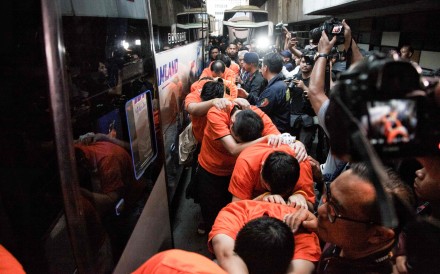 Suspected online gambling operators (in orange) walk towards buses for transfer after a police raid at the Hayam Wuruk Plaza office building in Jakarta on Sunday. Photo: AFP