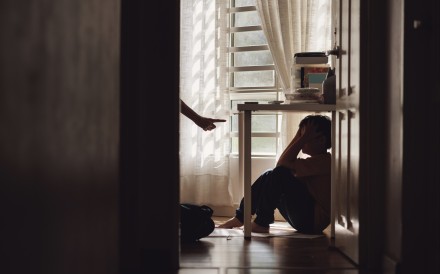 A little Asian boy with a sad and lonely expression hides in the shadows under a table at home, while being scolded by his mother. Photo: Getty Image
