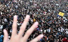 A man holds up his hand to symbolise the five demands of Hong Kong protesters as demonstrators protest in the background. Photo: AFP