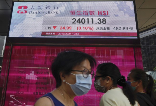 People walk past an electronic board showing the Hong Kong share index. Photo: AP