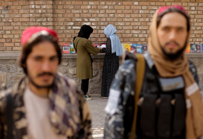 Two Taliban fighters and two girls at a book stall outside Kabul university. Photo: Reuters