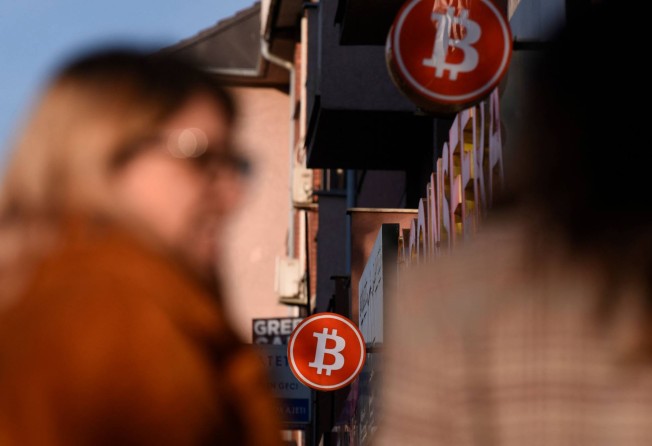 Pedestrians walk under a bitcoin cryptocurrency symbol displayed at a cryptocurrency exchange shop in Pristina, Kosovo, on January 17. Amid an energy crisis, Kosovo’s government brought in a temporary ban on cryptocurrency mining in an effort to bring down electricity consumption. Photo: AFP