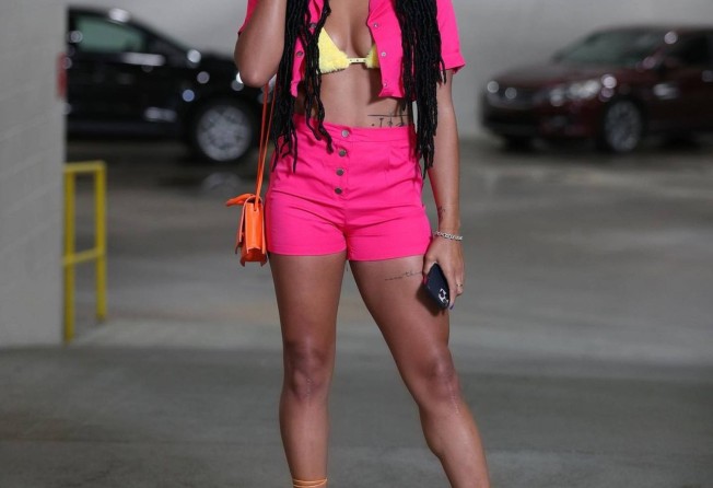 DiJonai Carrington wearing bright pink shorts and a matching crop jacket over a yellow bikini top with strappy sandals. Photo: Instagram