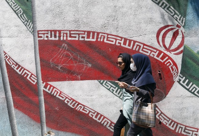 Iranian girls walk past a wall painting of Iran’s national flag in a street in downtown of Tehran. Photo: EPA-EFE