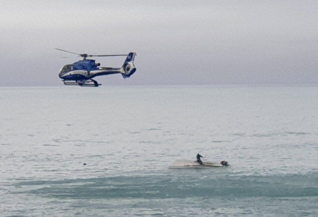A helicopter flies over an overturned boat with a survivor sitting on the hull off the coast of Kaikoura. Photo: AP