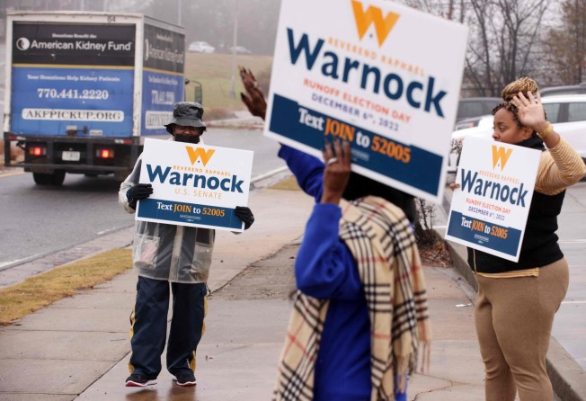 Supporters of US Senator Raphael Warnock hold signs by a road on Tuesday to encourage motorists to vote in the run-off election. Photo: Getty Images via AFP