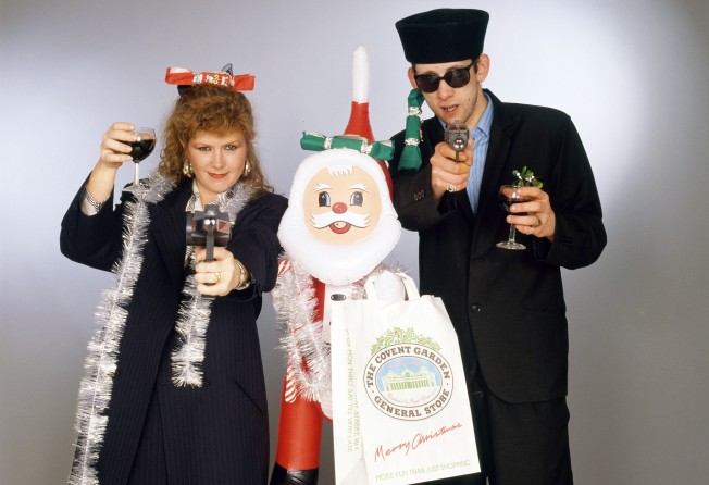 Singers Kirsty MacColl (1959–2000) and Shane MacGowan with toy guns and an inflatable Santa in a festive scenario, circa 1987. Photo: Getty Images