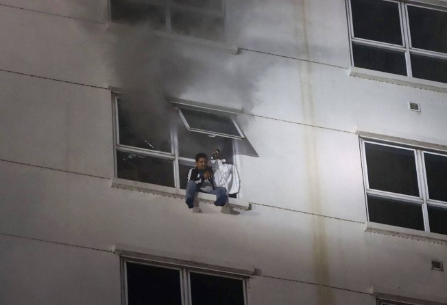A man sits on a window ledge as a fire burns through the Grand Diamond City hotel-casino. Photo: AFP