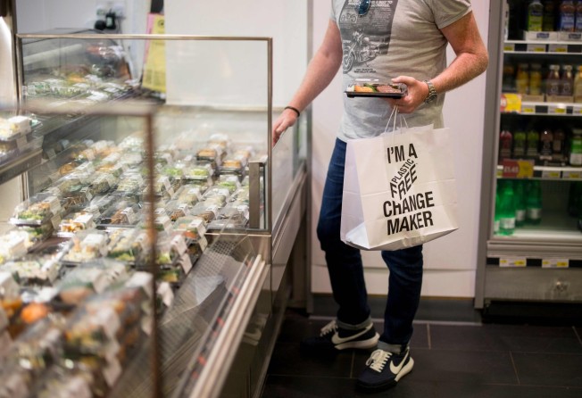 A shopper holds a paper bag with a slogan promoting plastic-free packaging. Under the new rules, retailers and restaurants will not be able to sell single-use plastic plates, trays and balloon sticks or some types of polystyrene cups and food containers. Photo: AFP